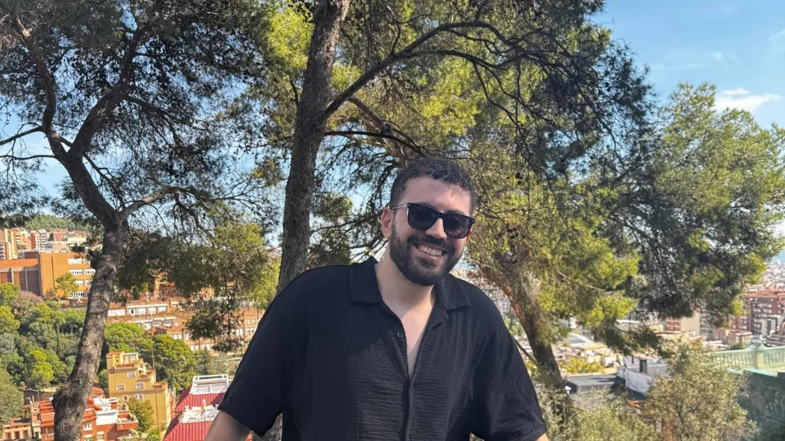 Abdelrahman smiling in front of pine trees and a city view
